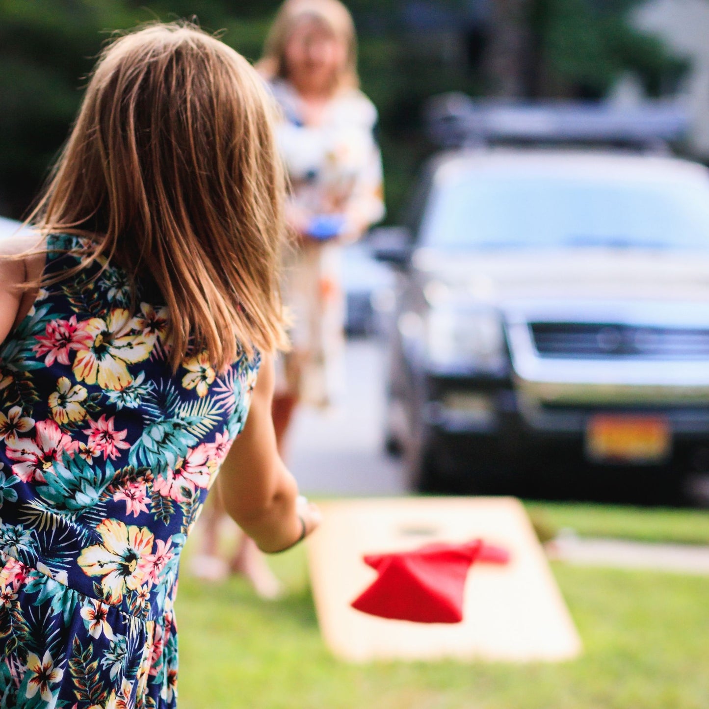 Woman throws cornhole bag at outdoor party rented cornhole set